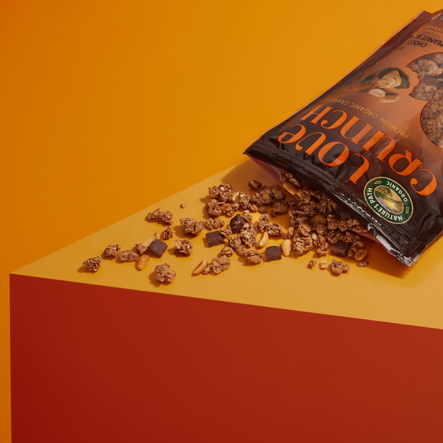 A bag of Nature's Path Love Crunch granola is tipped over, spilling its contents on a table top.