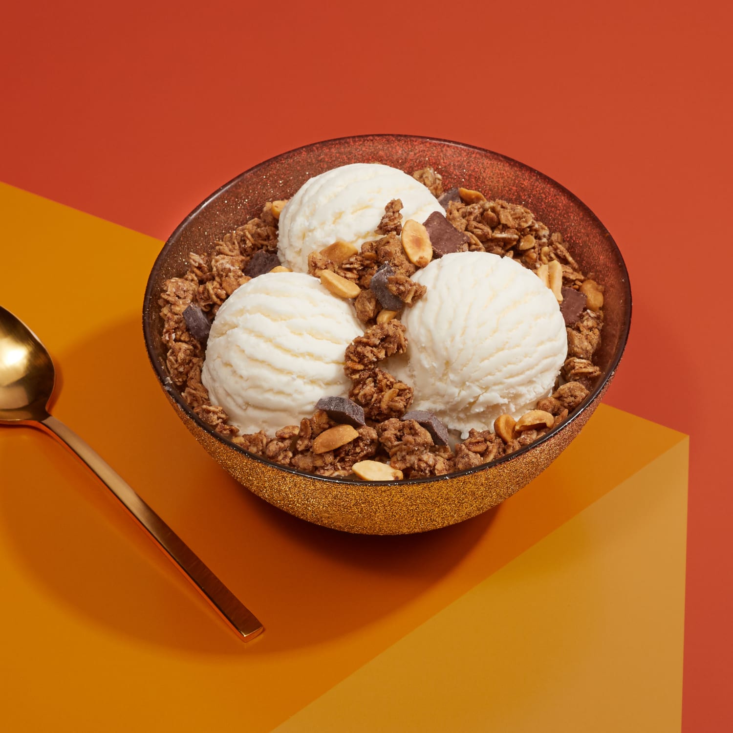 A bowl of three ice cream scoops topped with Love Crunch granola, placed on a table, with a spoon to the side.