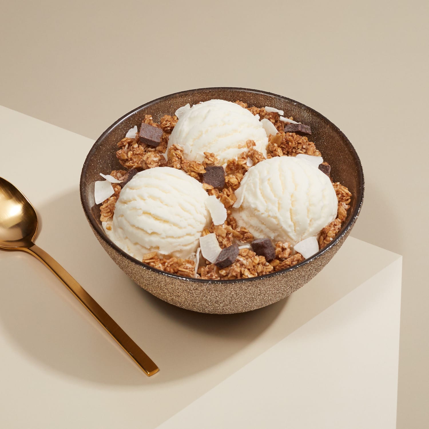 A bowl of three ice cream scoops topped with Love Crunch granola, placed on a table, with a spoon to the side.