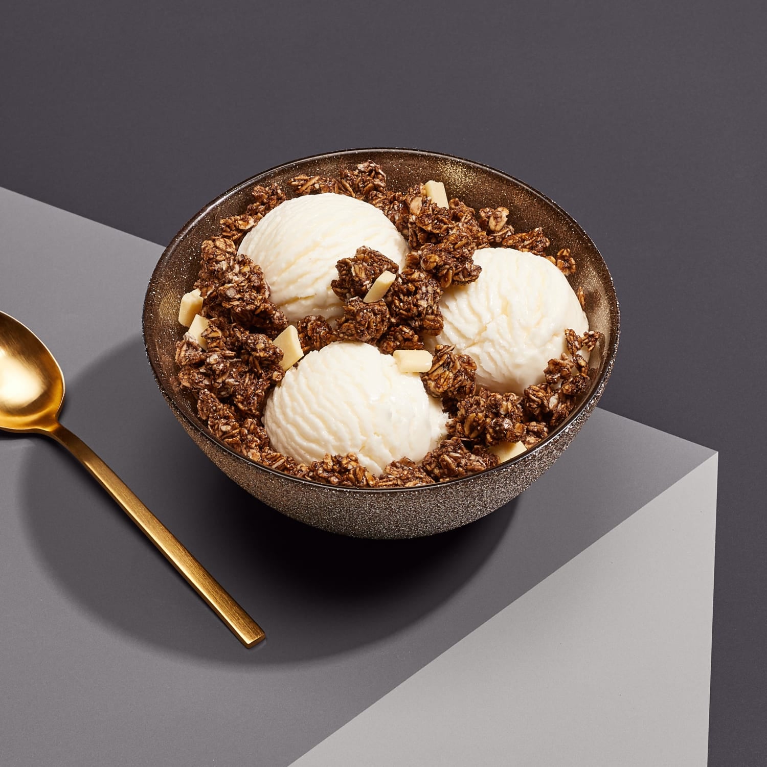 A bowl of three ice cream scoops topped with Love Crunch granola, placed on a table, with a spoon to the side.