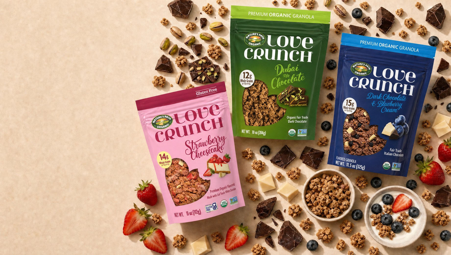 The three new Love Crunch granola flavors staged on cream paper with chocolate, pistachios, strawberries and blueberries